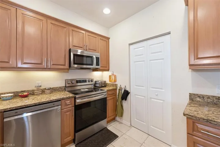 Kitchen with stainless steel appliances, dark stone counters, brown cabinets, and recessed lighting