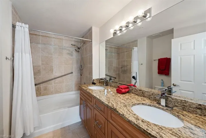 Full bathroom with double vanity, shower / tub combo with curtain, and light tile patterned flooring