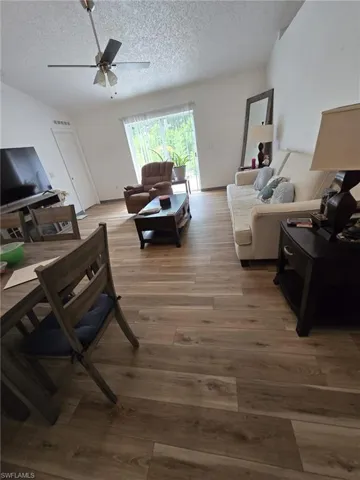 Living room featuring a textured ceiling, a ceiling fan, and light wood-style flooring