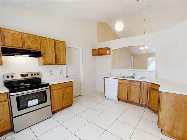 Kitchen with stainless steel electric range, under cabinet range hood, white dishwasher, a sink, and brown cabinets