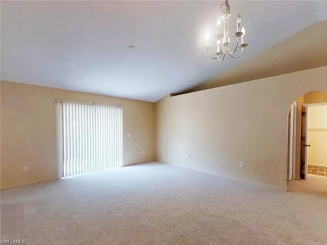 Unfurnished room with arched walkways, vaulted ceiling, carpet flooring, a chandelier, and baseboards