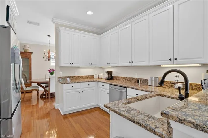 Kitchen featuring white cabinets, freestanding refrigerator, crown molding, light wood finished floors, and dark stone countertops