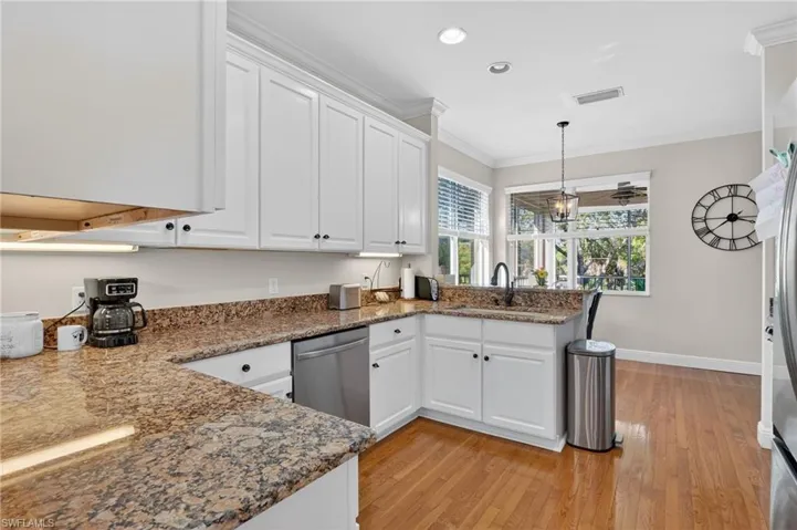 Kitchen featuring white cabinetry, a peninsula, ornamental molding, dark stone countertops, and light wood finished floors