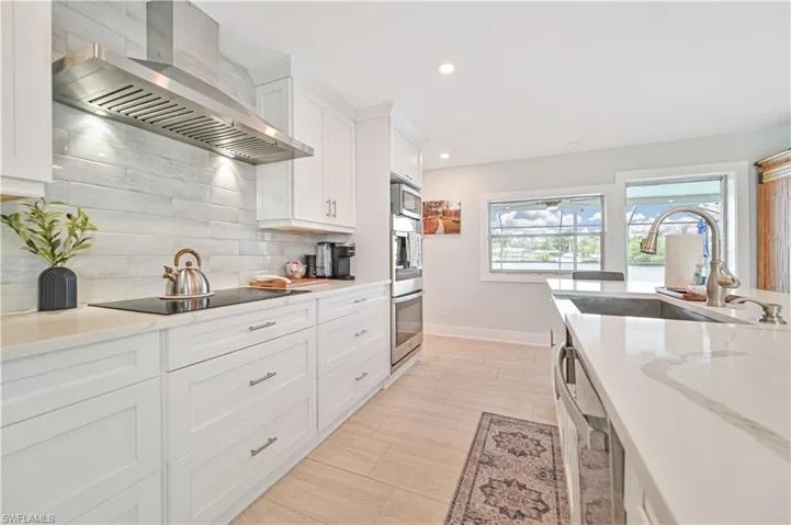 Kitchen with wall chimney exhaust hood, stainless steel appliances, decorative backsplash, white cabinetry, and recessed lighting