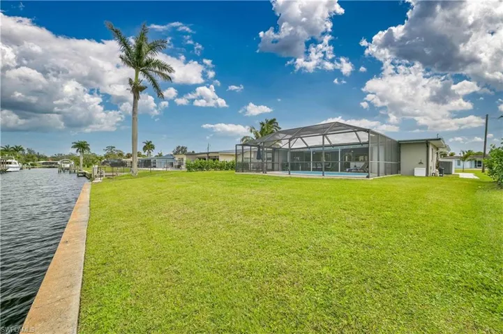View of green lawn with a lanai, a water view, and a boat dock