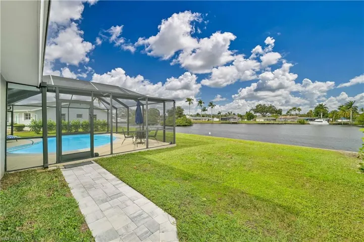 View of grassy yard with a water view, an outdoor pool, a patio area, and a lanai