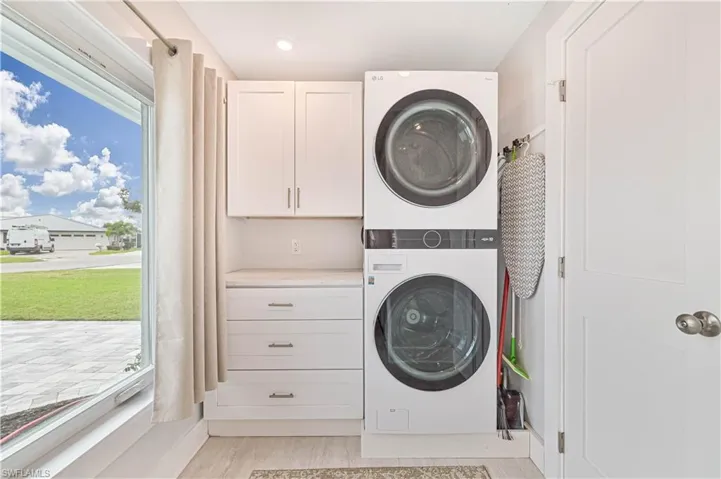 Laundry area featuring stacked washer and clothes dryer, cabinet space, light wood finished floors, and recessed lighting