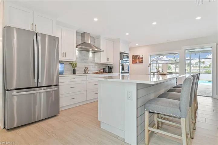 Kitchen with appliances with stainless steel finishes, wall chimney exhaust hood, a kitchen island with sink, light countertops, and tasteful backsplash