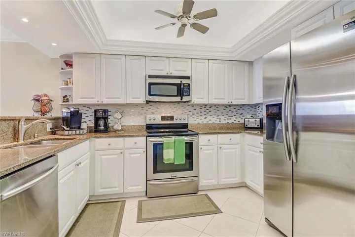Kitchen featuring stainless steel appliances, light stone counters, white cabinetry, ornamental molding, and a ceiling fan