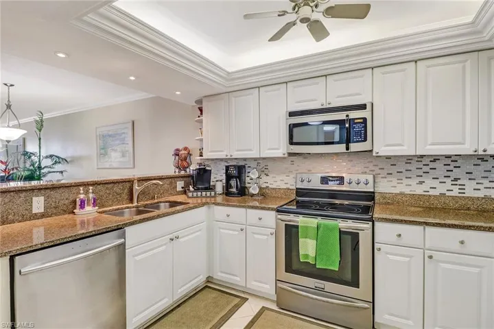 Kitchen featuring stainless steel appliances, ornamental molding, dark stone countertops, white cabinetry, and a raised ceiling