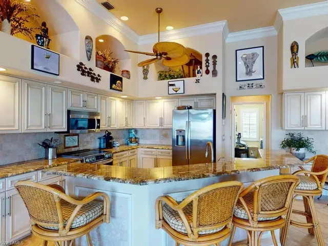Kitchen with a towering ceiling, appliances with stainless steel finishes, hanging light fixtures, ornamental molding, and a breakfast bar
