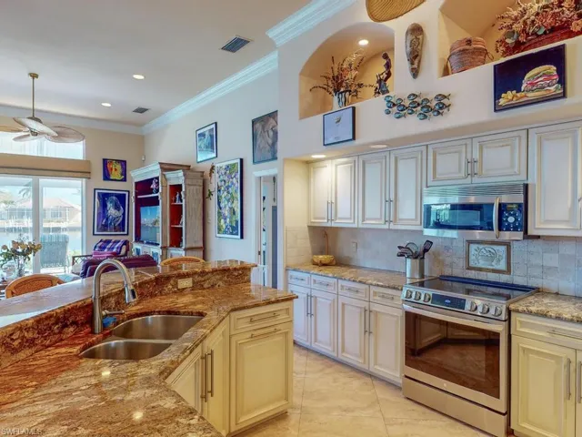 Kitchen featuring light stone countertops, stainless steel appliances, cream cabinets, and sink