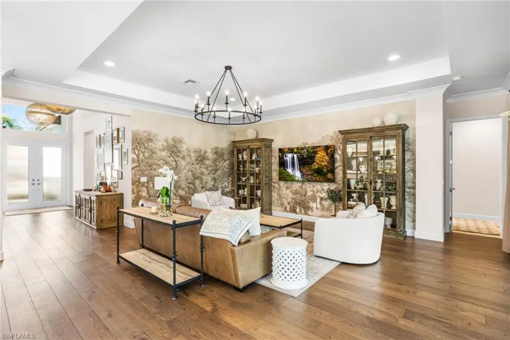 Living room with french doors, hardwood / wood-style floors, hanging lights, a tray ceiling, and ornamental molding