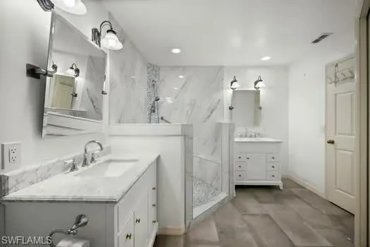 Full bath featuring two vanities, a marble finish shower, and recessed lighting