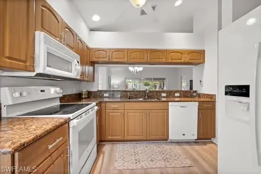 Kitchen featuring white appliances, a chandelier, recessed lighting, light wood finished floors, and dark stone countertops