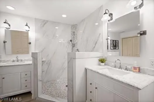 Bathroom featuring a marble finish shower, two vanities, and recessed lighting
