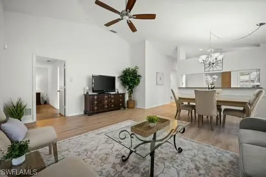Living room with light wood-style floors, ceiling fan, a chandelier, and high vaulted ceiling