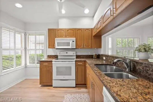 Kitchen featuring white appliances, healthy amount of natural light, recessed lighting, dark stone counters, and light wood-style flooring