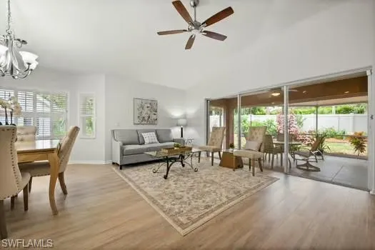 Living room with light wood-style flooring, a chandelier, ceiling fan, and vaulted ceiling