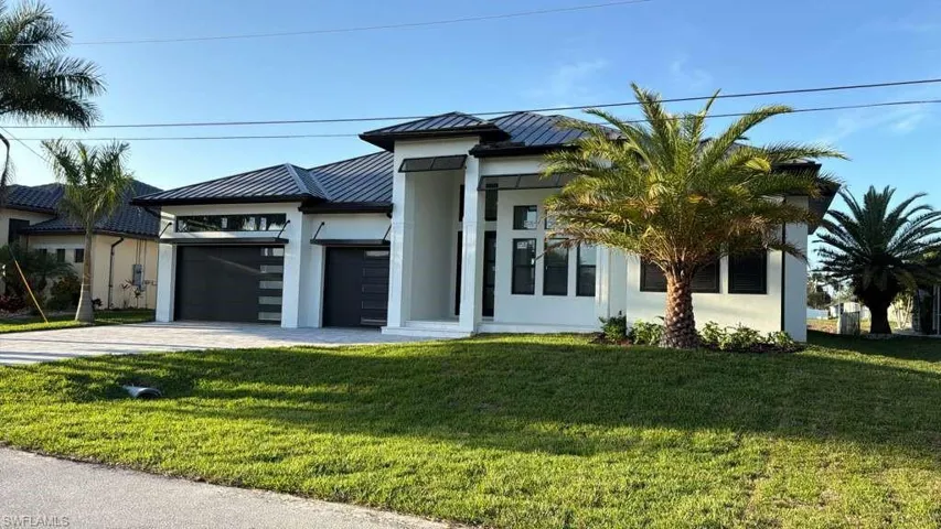 View of front of property featuring the landscape, driveway, a garage, stucco siding, and a standing seam roof