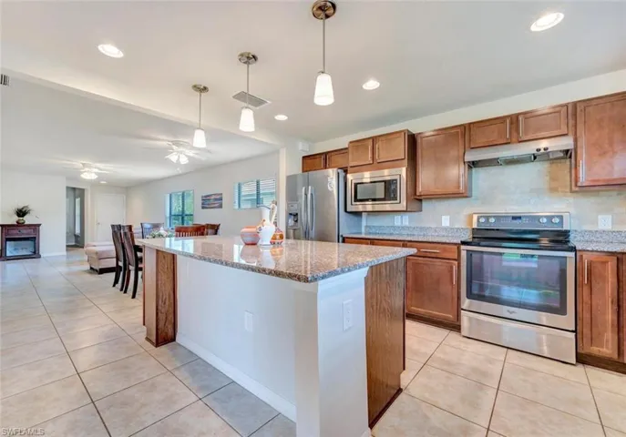Kitchen featuring a center island, hanging light fixtures, light stone countertops, stainless steel appliances, and ceiling fan