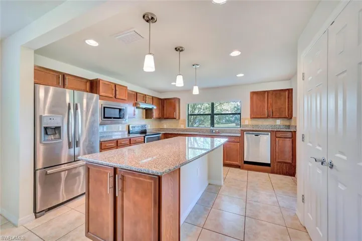 Kitchen with light tile flooring, stainless steel appliances, backsplash, hanging light fixtures, and a center island