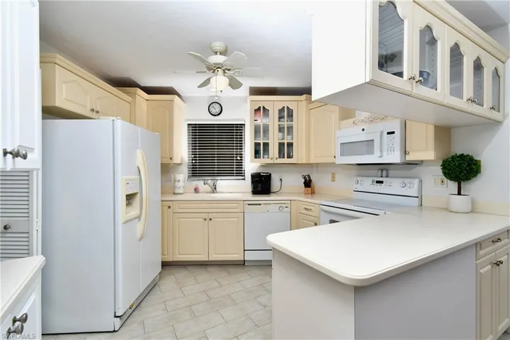 Kitchen with ceiling fan, kitchen peninsula, white appliances, light tile floors, and sink