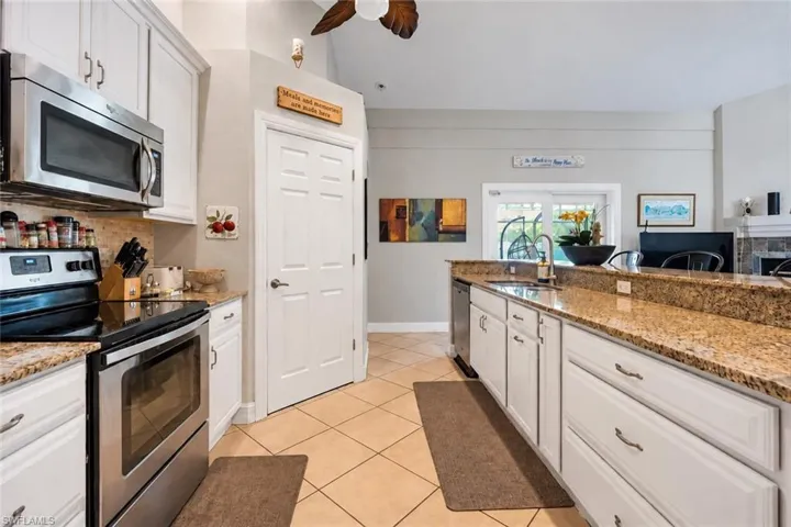 White cabinetry, stainless steel appliances, tile flooring, granite-finish countertops, and a ceiling fan with wood-finish blades