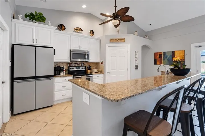 Kitchen featuring vaulted ceilings, white cabinetry, integrated stainless steel appliances, a breakfast bar with stone-finish countertop, and tile flooring