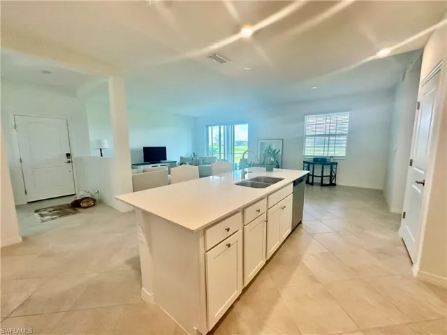 Kitchen with white cabinets, a kitchen island with sink, stainless steel dishwasher, open floor plan, and light tile patterned flooring