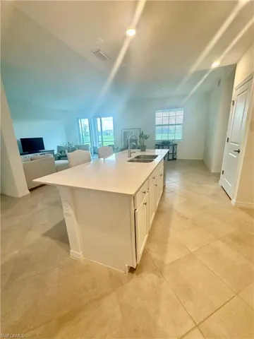 Kitchen featuring open floor plan, white cabinetry, a center island with sink, light stone countertops, and light tile patterned floors