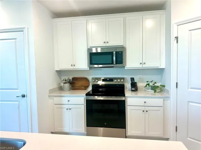 Kitchen featuring stainless steel appliances, white cabinets, and light stone countertops