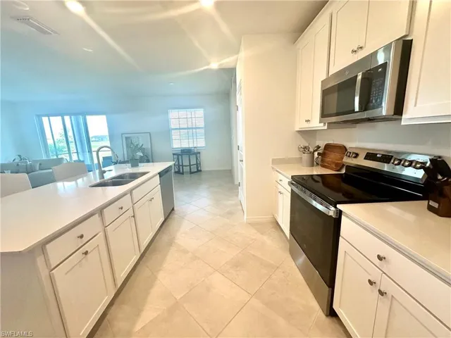 Kitchen with appliances with stainless steel finishes, white cabinetry, open floor plan, and a center island with sink