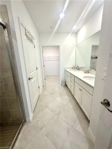 Full bathroom featuring a walk in closet, a stall shower, and double vanity
