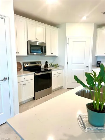 Kitchen with stainless steel appliances, light tile patterned flooring, white cabinets, and light stone counters