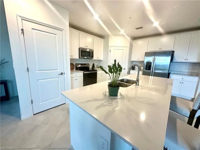 Kitchen featuring white cabinetry, stainless steel appliances, a kitchen island with sink, light stone countertops, and light tile patterned floors