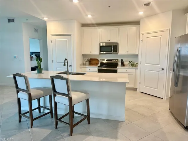 Kitchen with appliances with stainless steel finishes, white cabinets, a breakfast bar, an island with sink, and recessed lighting