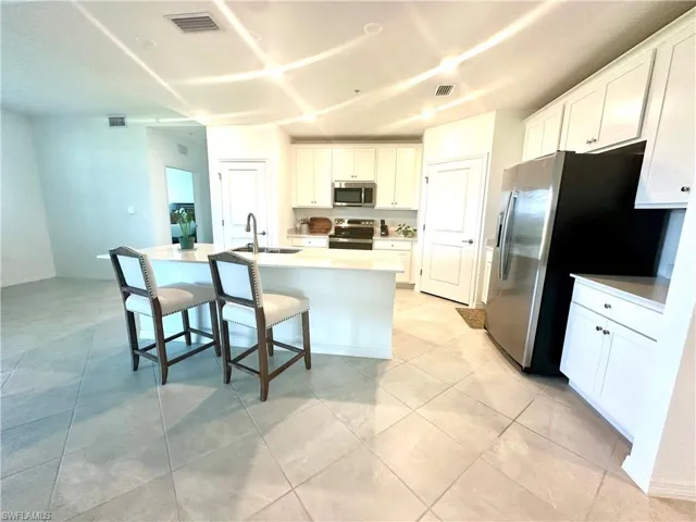 Kitchen featuring white cabinetry, appliances with stainless steel finishes, a kitchen breakfast bar, a center island with sink, and light tile patterned flooring
