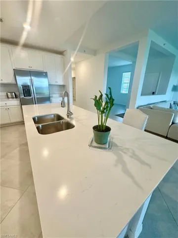 Kitchen with stainless steel refrigerator with ice dispenser, light stone counters, white cabinets, light tile patterned flooring, and a breakfast bar area