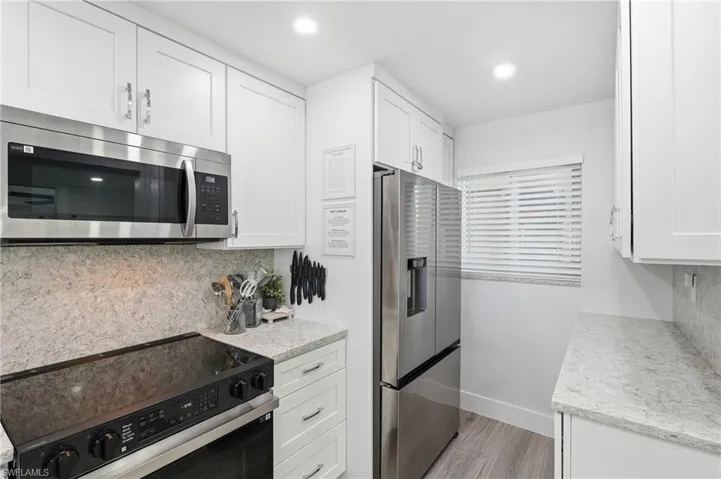 White shaker cabinetry, stainless steel appliances, speckled countertops, coordinating backsplash, and wood-finish flooring - Virtually Edited Image