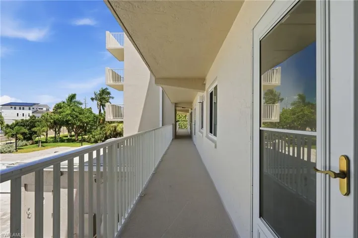 Exterior walkway featuring a metal railing, multiple windows, and an entry door with a brass-finish handle - Virtually Edited Image