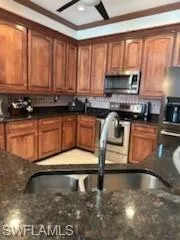 Kitchen featuring backsplash, stove, crown molding, dark stone countertops, and sink