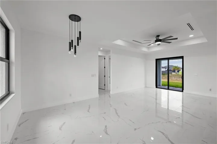 Empty room with baseboards, a ceiling fan, a tray ceiling, and marble finish floor