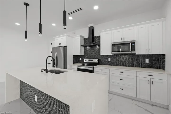 Kitchen with white cabinets, appliances with stainless steel finishes, a sink, marble finish floor, and wall chimney exhaust hood