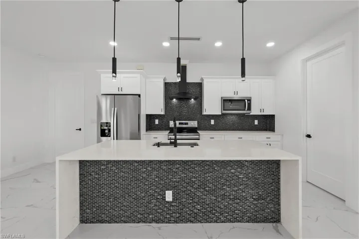 Kitchen with marble finish floor, wall chimney exhaust hood, a kitchen island with sink, and stainless steel appliances
