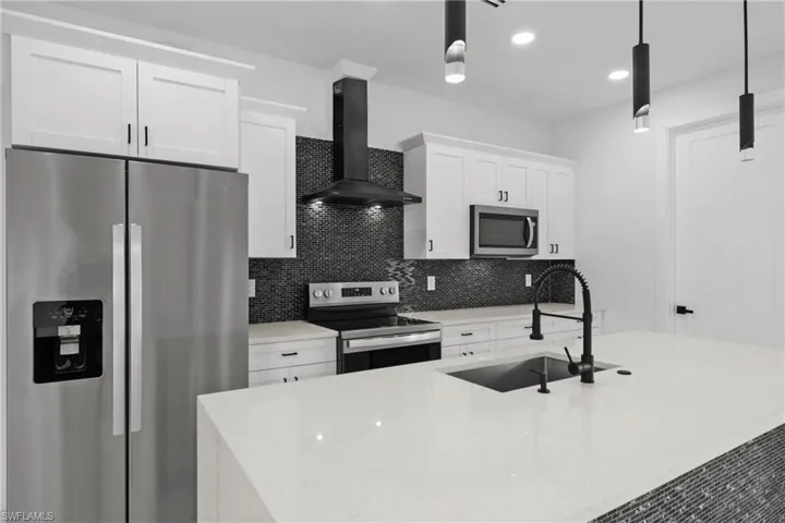 Kitchen featuring an island with sink, wall chimney range hood, white cabinetry, a sink, and appliances with stainless steel finishes
