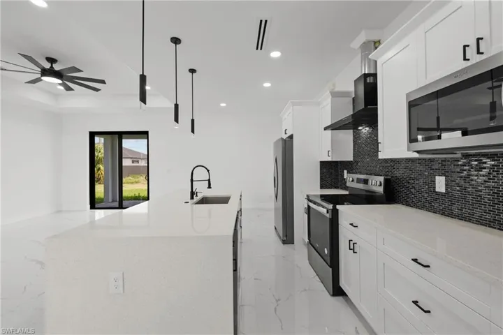 Kitchen with wall chimney range hood, appliances with stainless steel finishes, a sink, marble finish floor, and recessed lighting