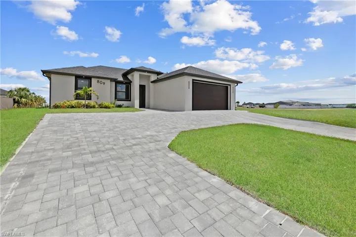 Prairie-style home with decorative driveway, an attached garage, a front yard, and stucco siding