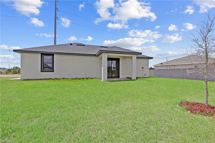 Rear view of house with a lawn, fence, and stucco siding