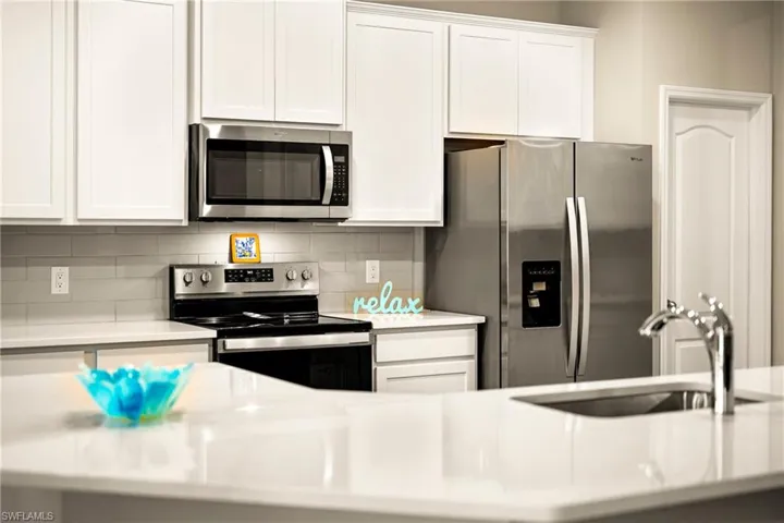 Kitchen with stainless steel appliances, white cabinets, light stone counters, and tasteful backsplash
